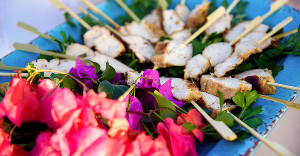 Chicken skewers served on blue platter with decorative tropical pink flowers