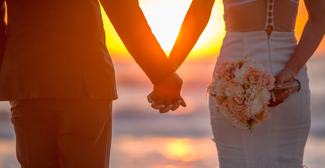 Bride and groom hold hands at sunset on beach