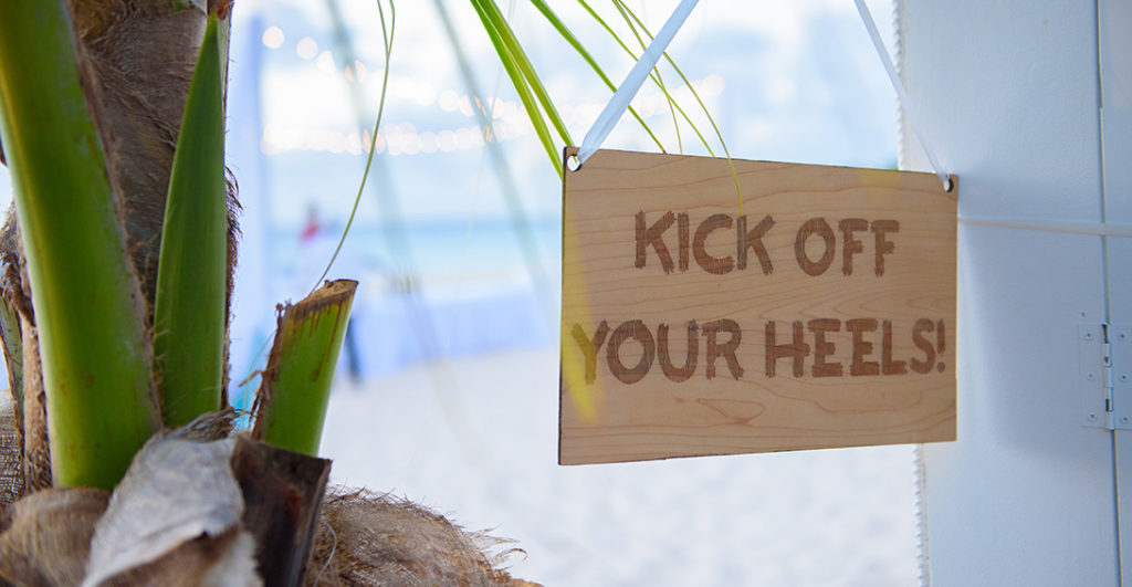 Decorative sign hanging on beach says "kick off your heels"