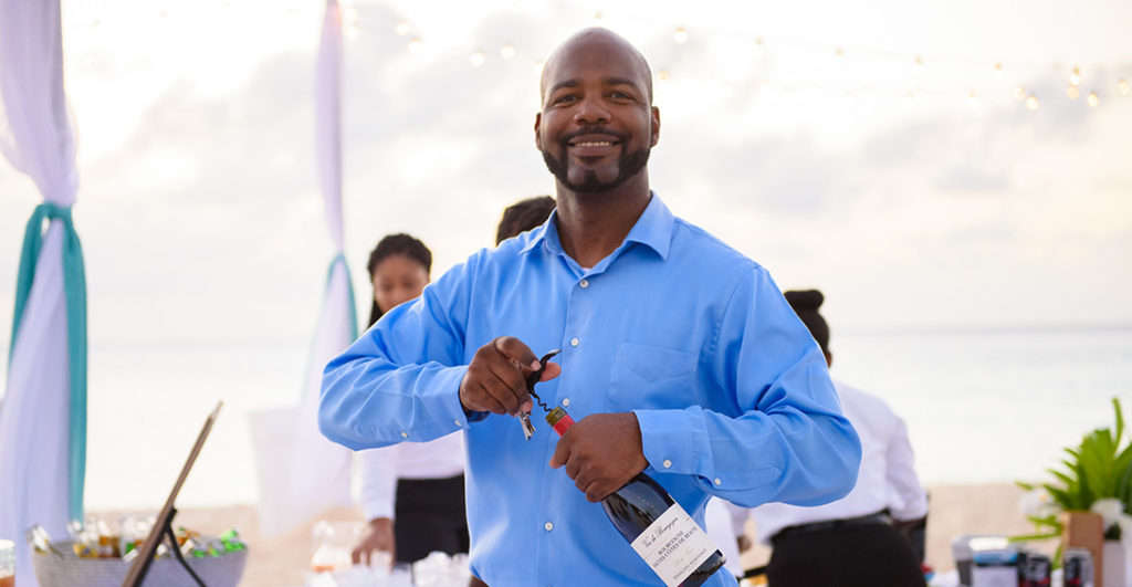 Blanchards bartender opens bottle of wine at private bar on beach